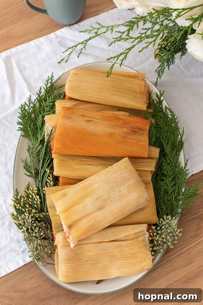 Beautifully arranged tamales on a green and white platter, garnished with festive Christmas greens.