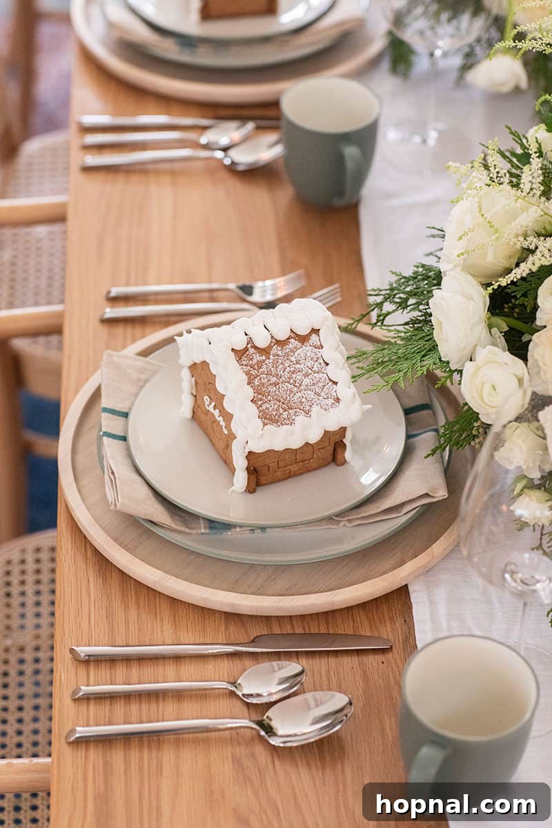 A small gingerbread house resting on a festive napkin and elegant dinner plates from Bed Bath & Beyond.