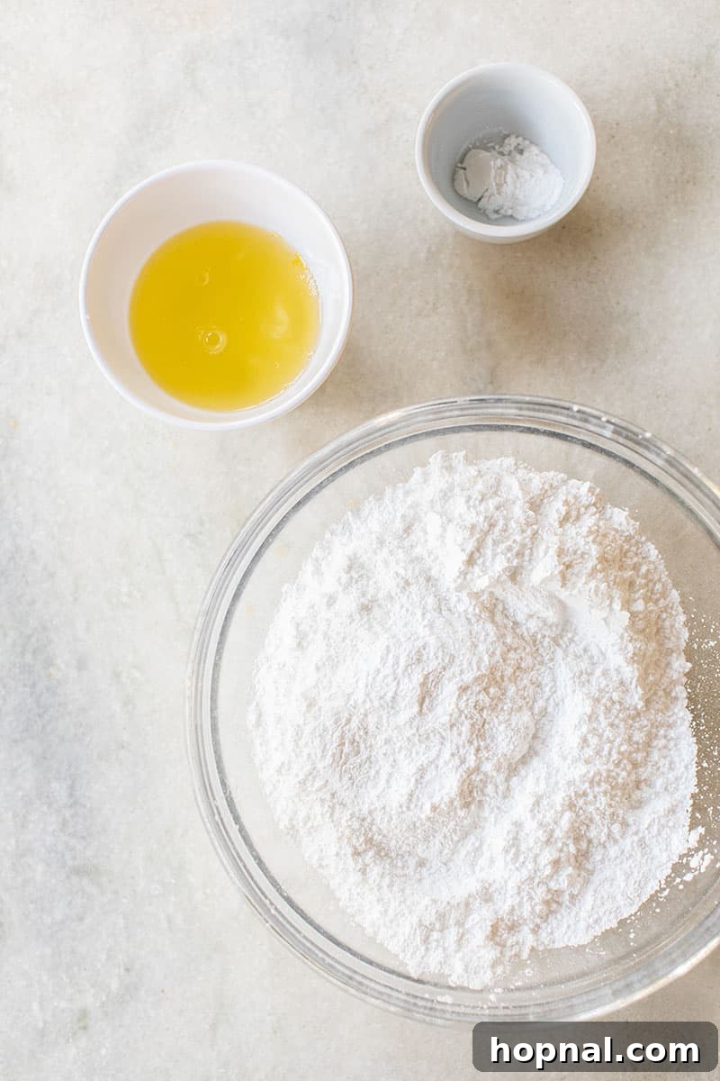 Close-up shot of egg whites, cream of tartar, and powdered sugar, the three essential ingredients for making the best gingerbread house icing.