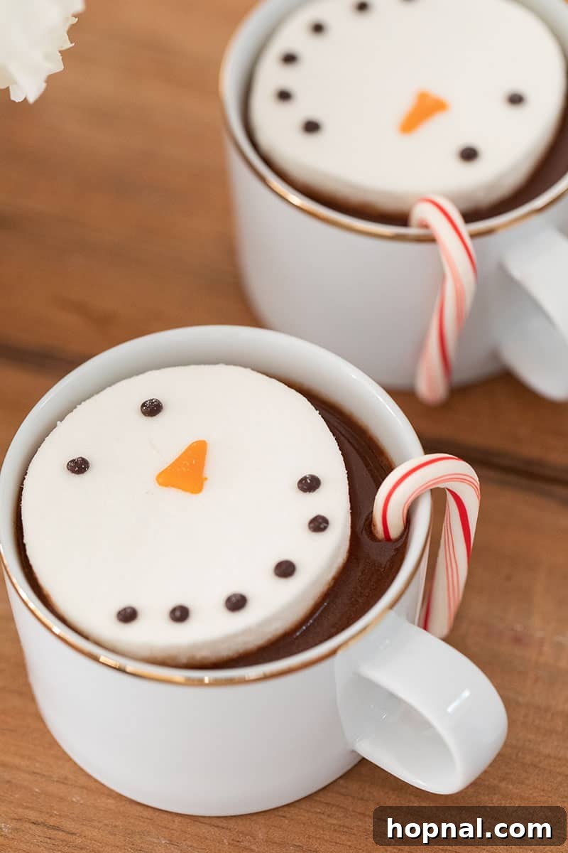 The Ultimate Guide to a Showstopping Christmas Dessert Display 18 Close-up of hot chocolate in white and gold mugs, each topped with a charming marshmallow snowman.