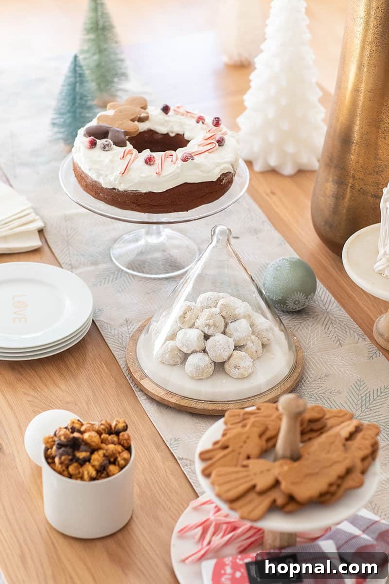 The Ultimate Guide to a Showstopping Christmas Dessert Display 3 Festive Christmas dessert table with a blue table runner, various snowball cookies, gingerbread cake, and decorated gingerbread cookies.