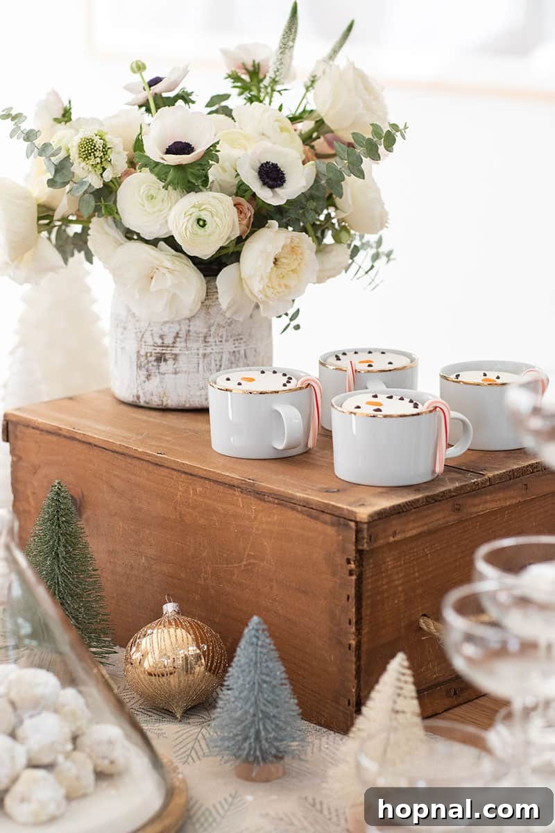 The Ultimate Guide to a Showstopping Christmas Dessert Display 4 Close-up of elegant gold cups filled with rich hot chocolate, topped with adorable snowman marshmallows, next to white floral arrangements.