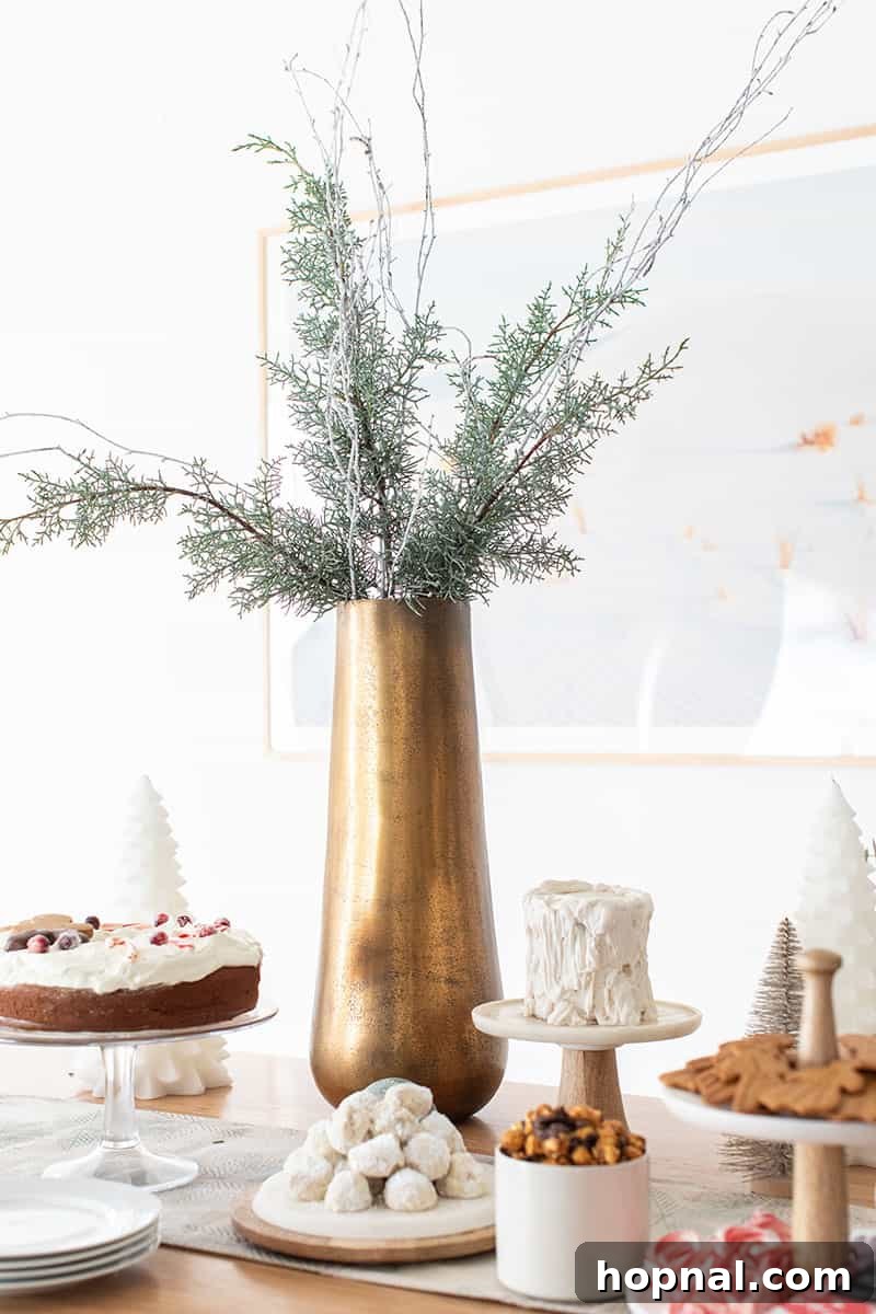 The Ultimate Guide to a Showstopping Christmas Dessert Display 9 A tall, elegant brass vase filled with lush green and white faux snowy branches, serving as a sophisticated centerpiece.