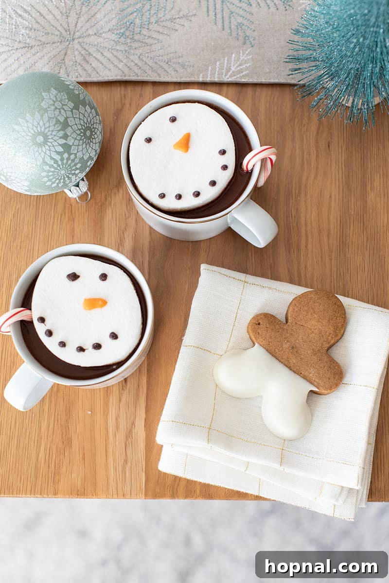 The Ultimate Guide to a Showstopping Christmas Dessert Display 10 Table setting with hot chocolate and snowman marshmallows, a gingerbread cookie on a white and gold napkin, and a sage ornament for festive detail.