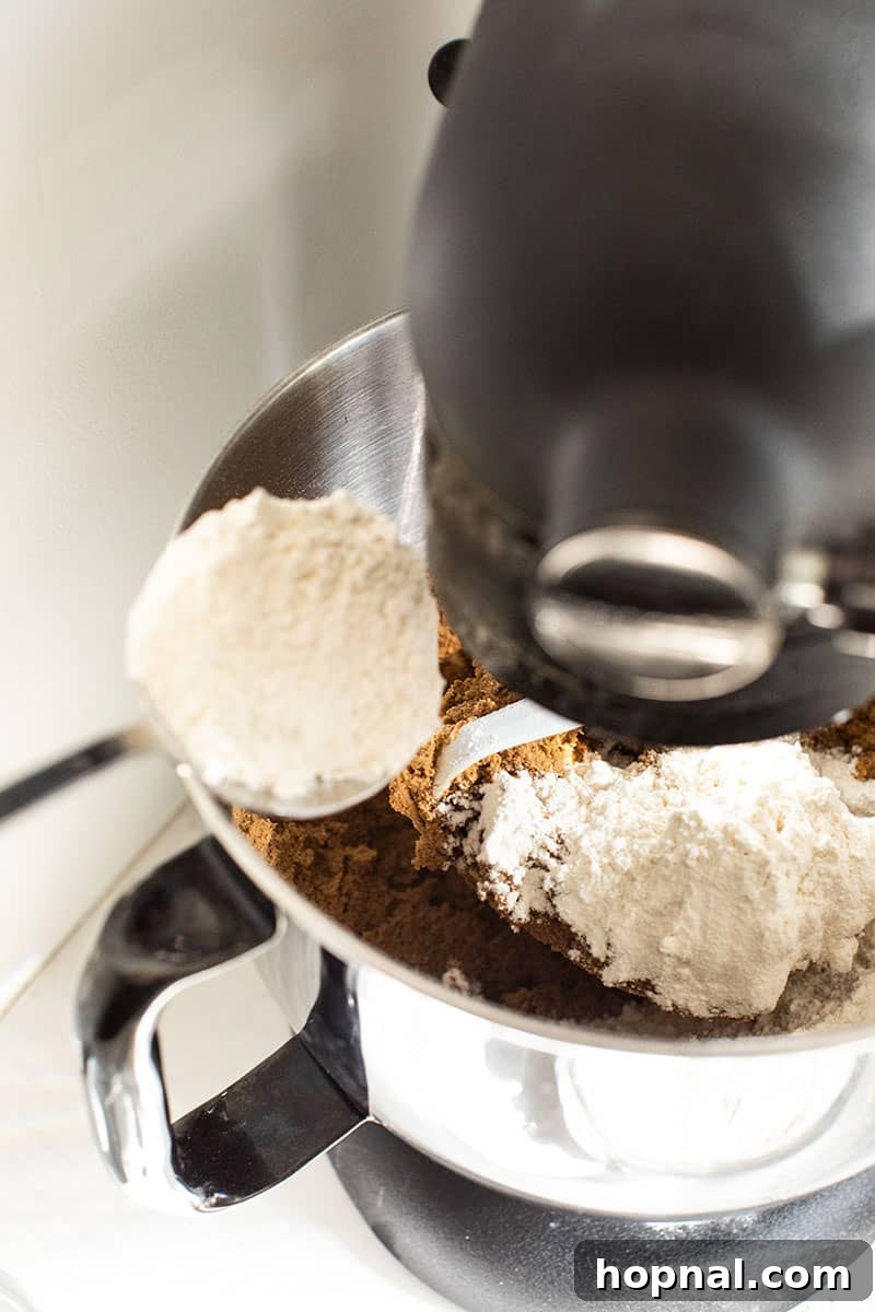 Adding flour gradually to the gingerbread dough in an electric mixer to achieve the right consistency.