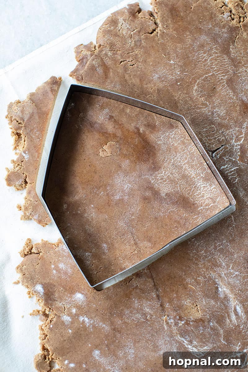 Freshly made gingerbread dough rolled out on a floured surface next to gingerbread house cookie cutters, ready for cutting.