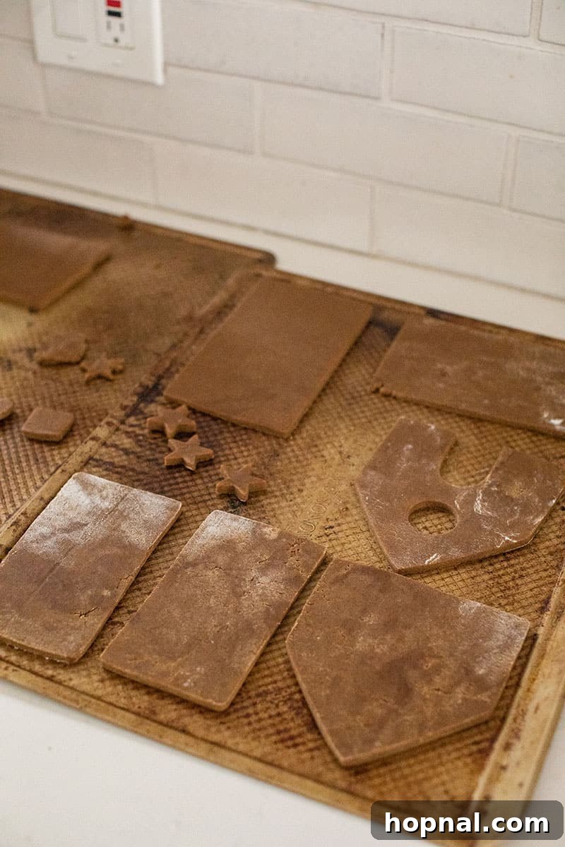 Cut gingerbread house pieces arranged on a parchment-lined baking sheet, waiting to be baked to a perfect golden crisp.
