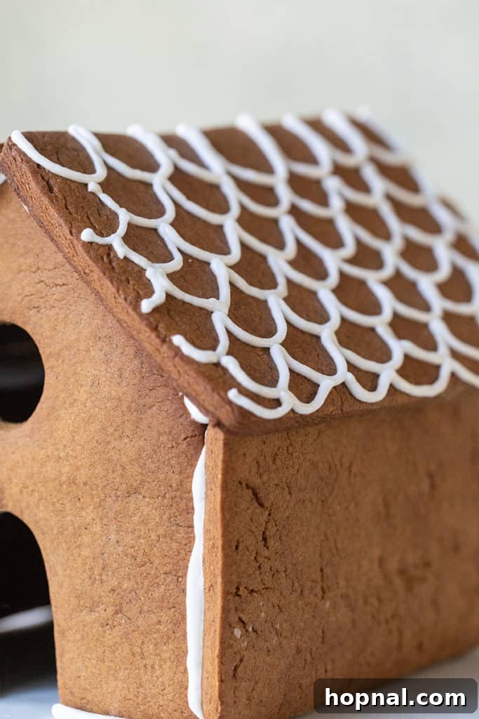 A partially decorated gingerbread house, showcasing intricate piping details and colorful candy embellishments on its walls.