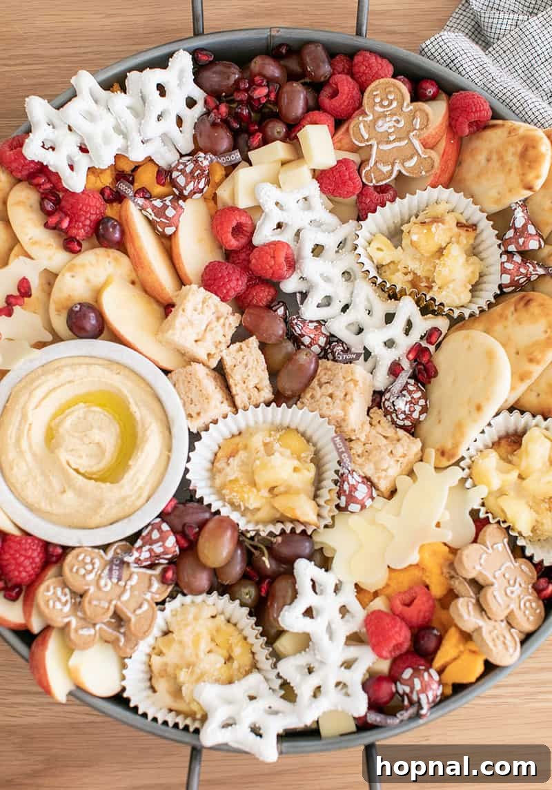 Santa's Snack Tray for Kids 5 A festive round tray thoughtfully arranged with a diverse selection of Christmas appetizers for kids, including creamy hummus, various cheeses, fresh berries, and delightful cookies, creating an ideal holiday spread.