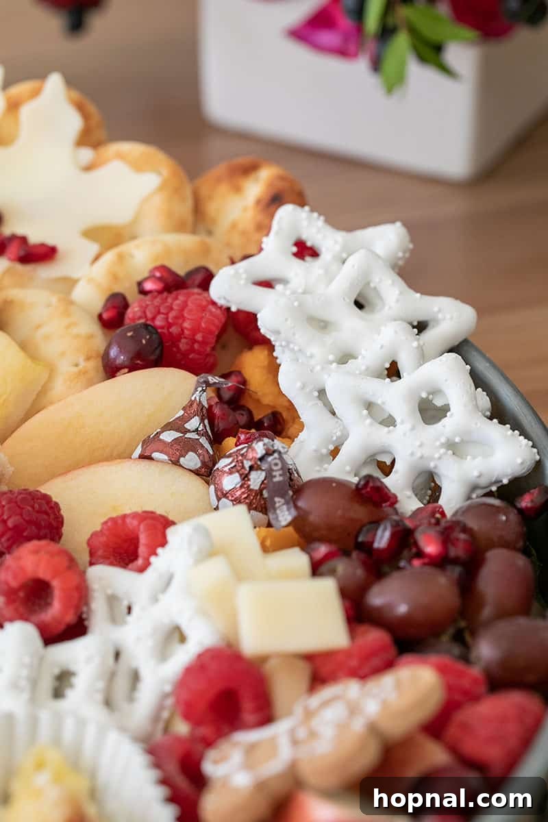 Santa's Snack Tray for Kids 7 A beautifully arranged round tray showcasing an inviting assortment of festive snacks: sweet yogurt-covered pretzels, juicy grapes, savory cheese cubes, crisp apple slices, and soft pita bread, ideal for a kids' holiday party.