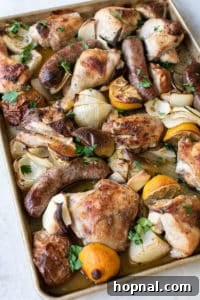 Chicken, sausage, apples, onions, and lemons baking on one sheet pan in the oven.