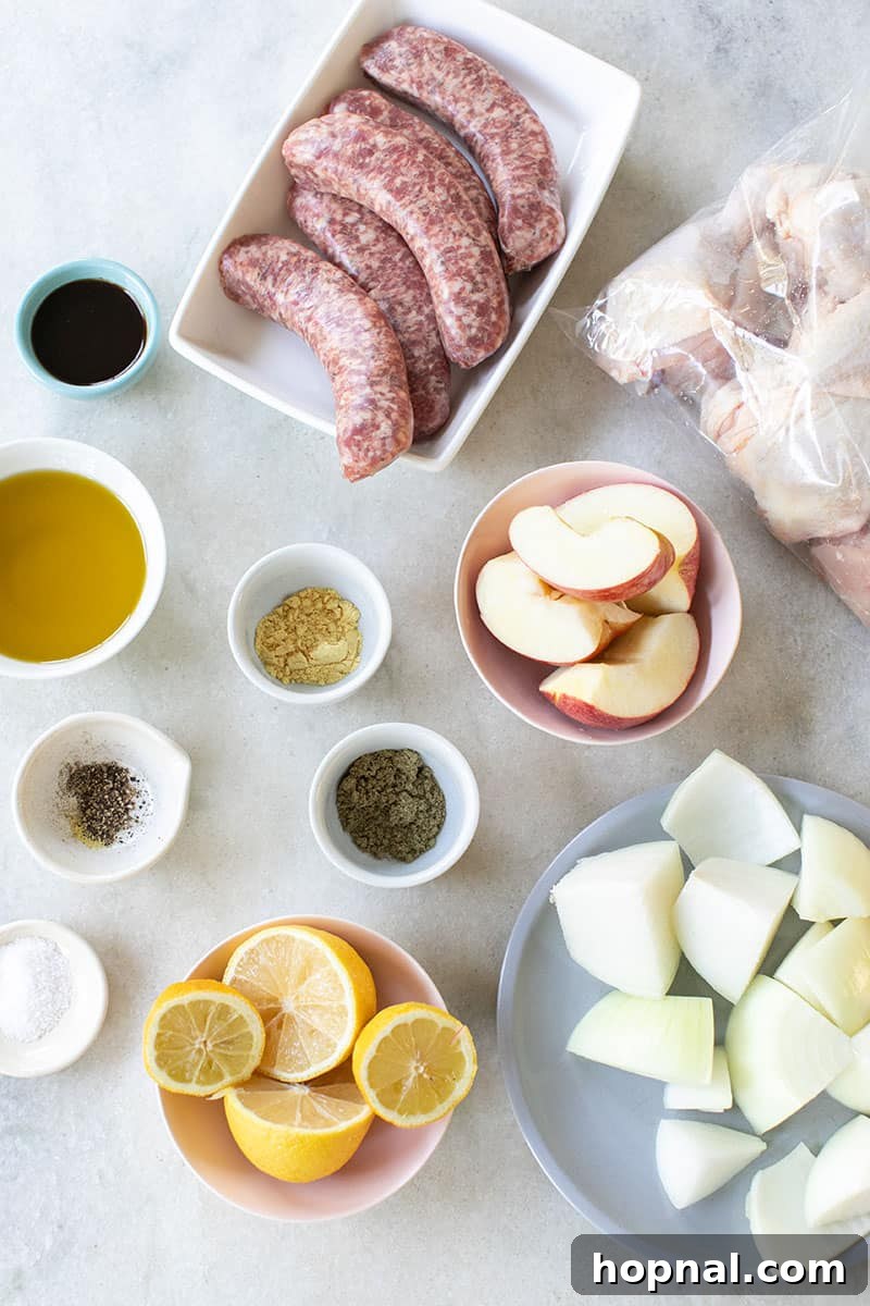 Fresh ingredients laid out on a marble countertop for a One-Pan Chicken and Sausage Bake, including chicken, sausage, lemons, apples, and spices.
