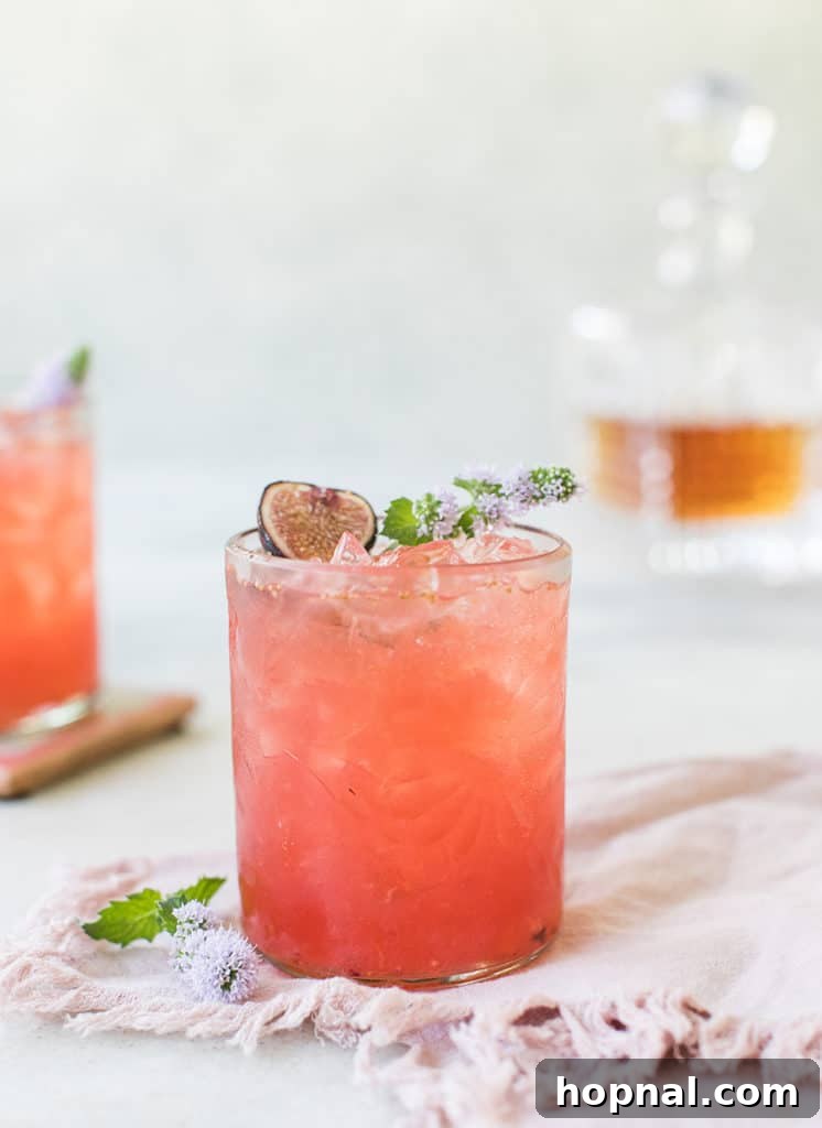 A refreshing Fig Sidecar cocktail presented with a pink bowl and pretty flowers in the background.