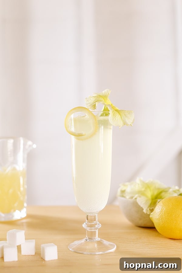 A classic French 75 cocktail garnished with a delicate lemon rind and a beautiful yellow flower.