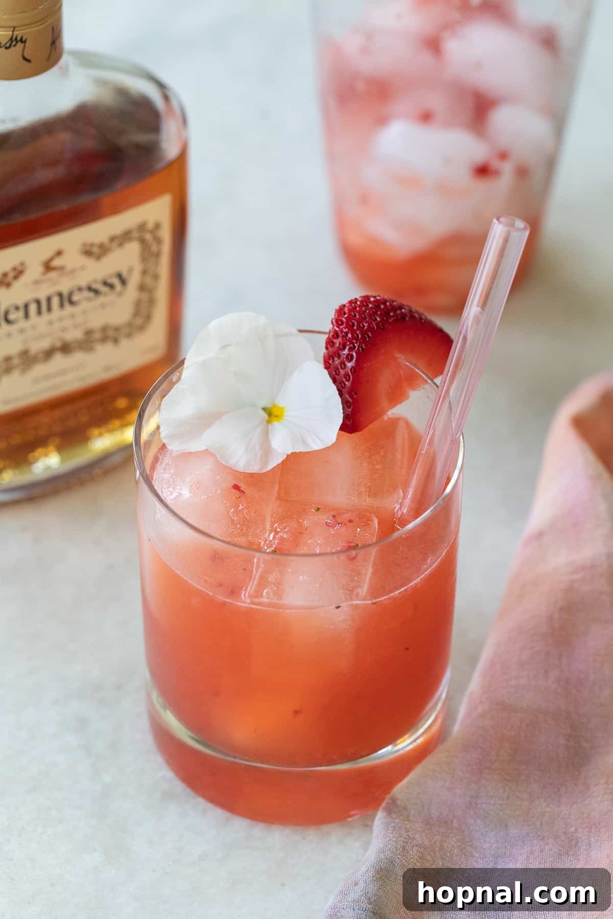 A charming Strawberry Hennessy drink garnished with a delicate white flower and a straw.