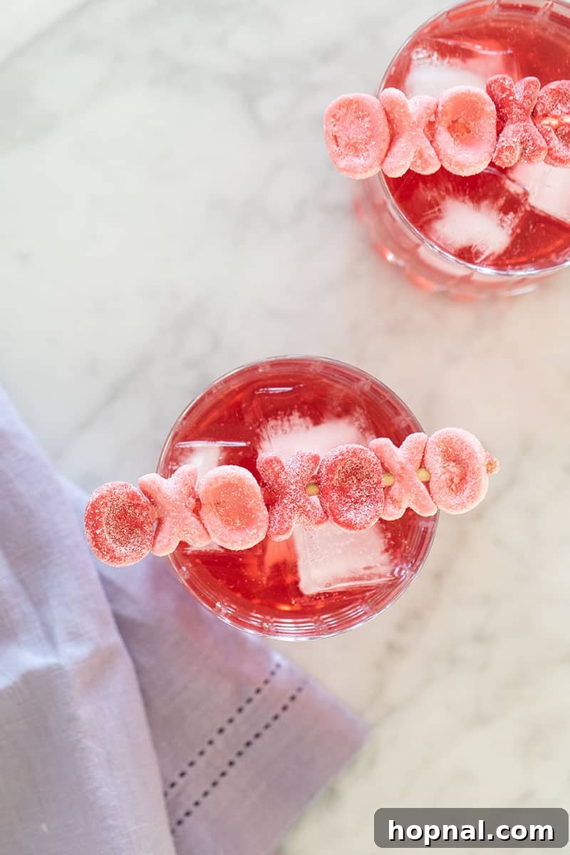 A Valentine's Day cocktail with an 'XOXO' drink stirrer, featuring a triple berry martini and a pretty pink drink.