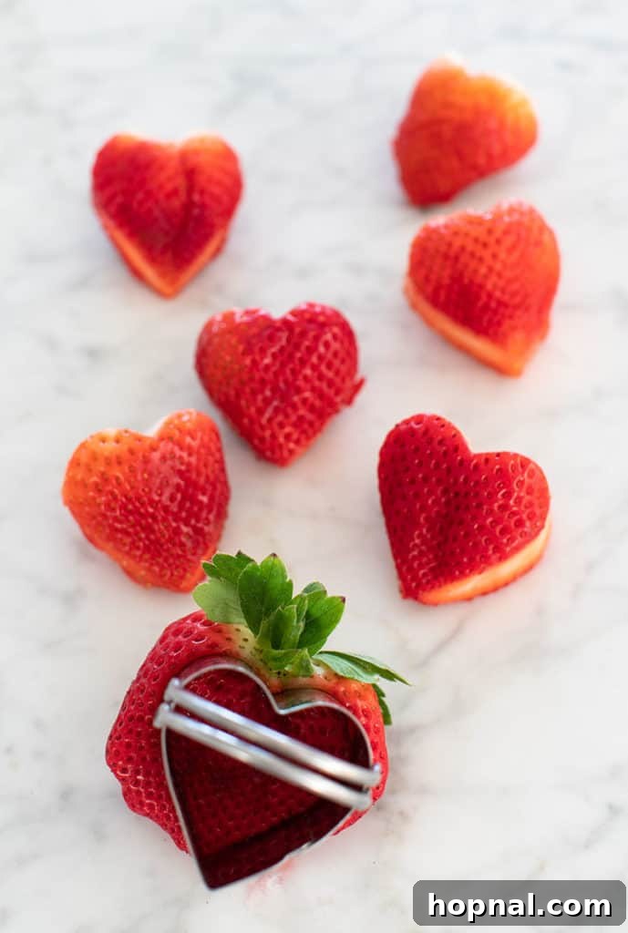 Valentine's Day Sweetheart's Grazing Board 18 A close-up shot of a strawberry being carefully pressed with a heart-shaped cookie cutter, showing the process of creating decorative fruit for a special occasion.