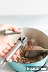 Adding garlic into a soup with a garlic press.