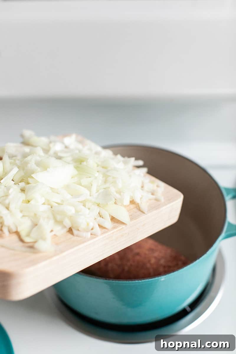 Hominy Soup The Ultimate Winter Comfort 5 Adding finely chopped onions into a Dutch oven where pork sausage is browning, beginning the aromatic foundation of the stew.
