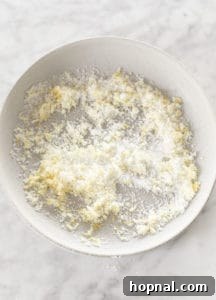 Lemon zest being rubbed into granulated sugar in a shallow dish, preparing a fragrant lemon sugar rim for a martini glass.