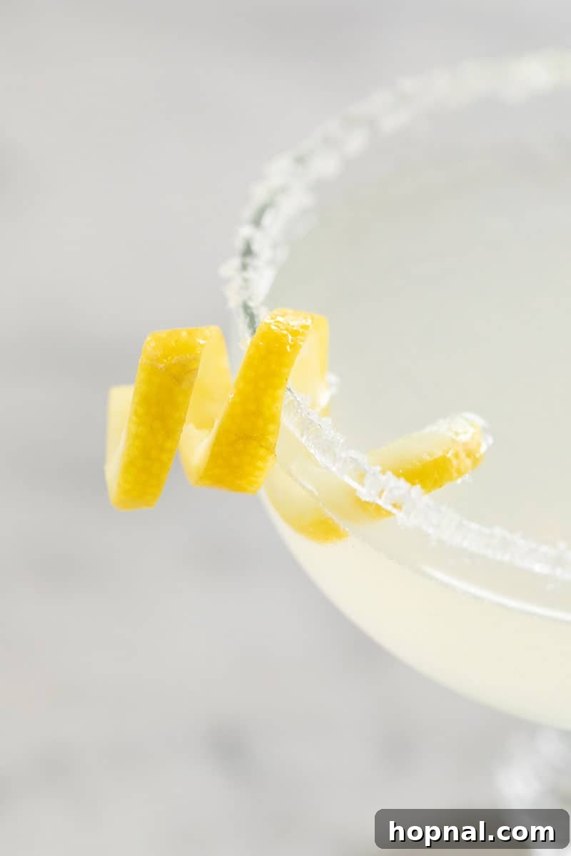 A vibrant Lemon Drop Martini, elegantly presented with a perfectly crafted lemon twist and a delicate sugared rim, on a light background.