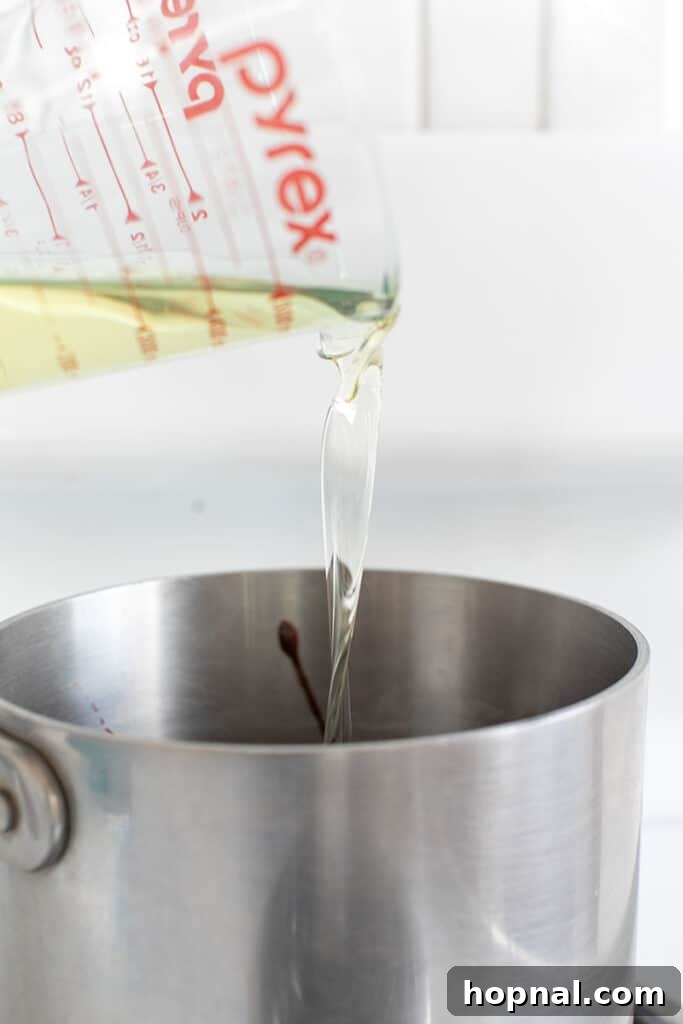 Pouring neutral cooking oil into a saucepan, already containing melted chocolate and butter, ensuring a perfectly moist and fudgy brownie texture.