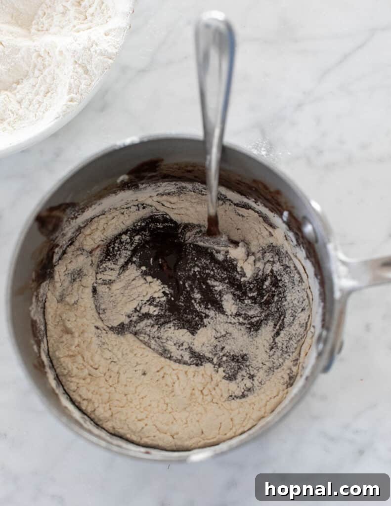 Gently folding all-purpose flour into the rich chocolate batter, being careful not to overmix to maintain the fudgy consistency of the brownies.