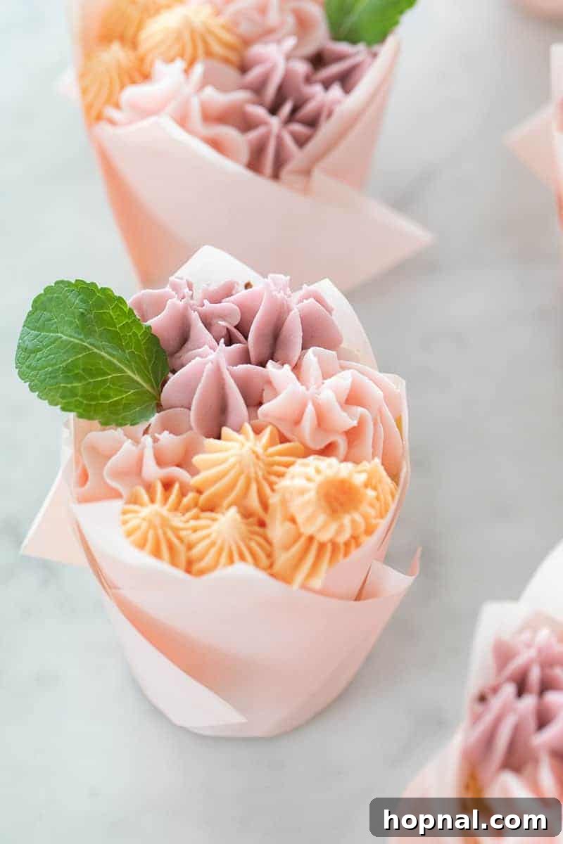 A beautifully decorated cupcake featuring small, intricate buttercream flowers and a tiny mint leaf, close-up.