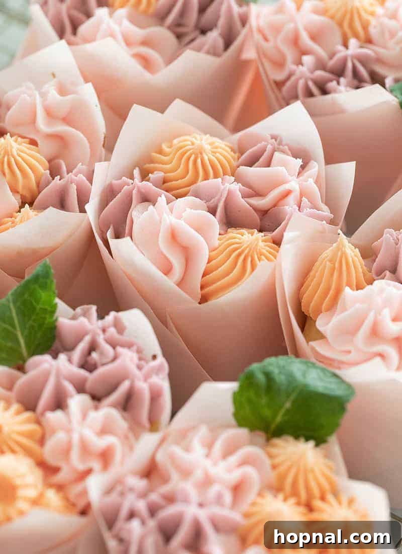 Close-up of a delicate buttercream flower cupcake nestled in a tulip wrapper, adorned with tiny fresh mint leaves.