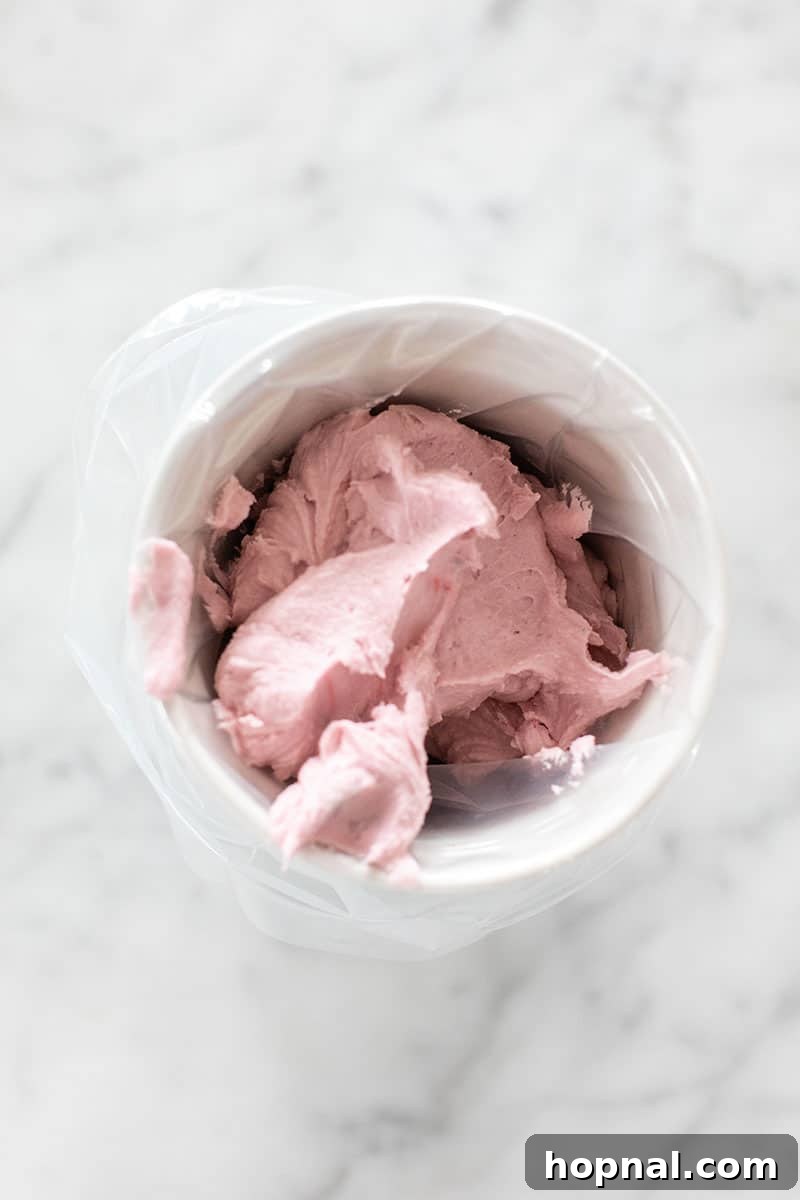 A piping bag positioned inside a tall glass, with the edges wrapped around the rim, ready to be filled with buttercream frosting.