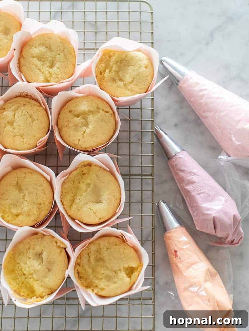 A collection of baked yellow cupcakes alongside three piping bags filled with different colored buttercream frosting, ready for decorating.
