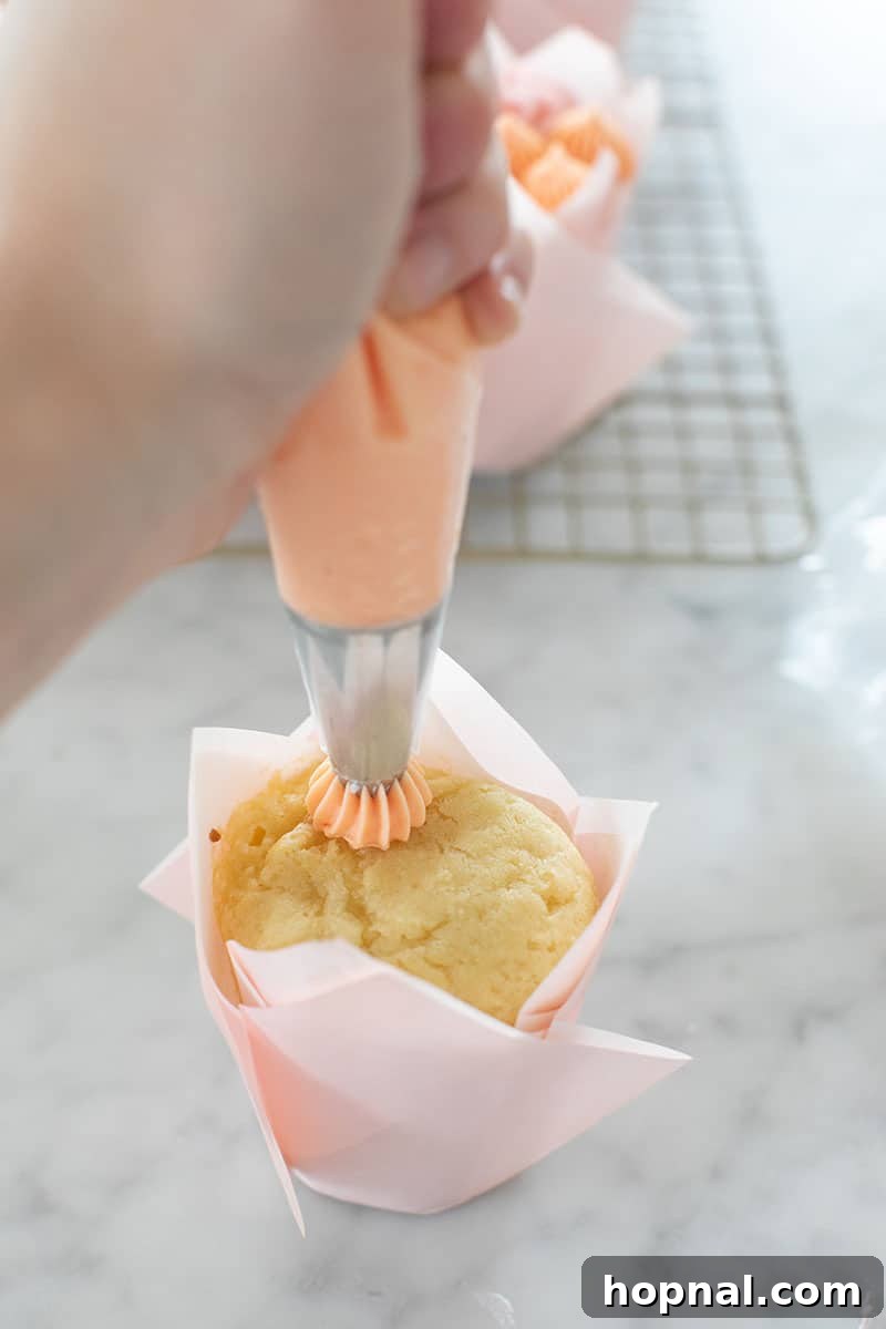 A hand demonstrating how to pipe a delicate buttercream flower onto a cupcake using a piping bag.