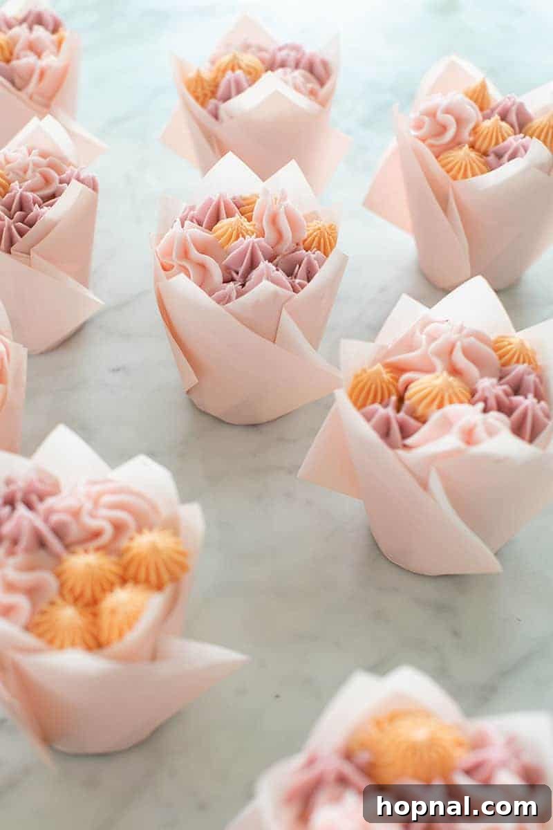 A close-up view of delicate floral cupcakes adorned with pink buttercream flowers and elegant green tulip wrappers.