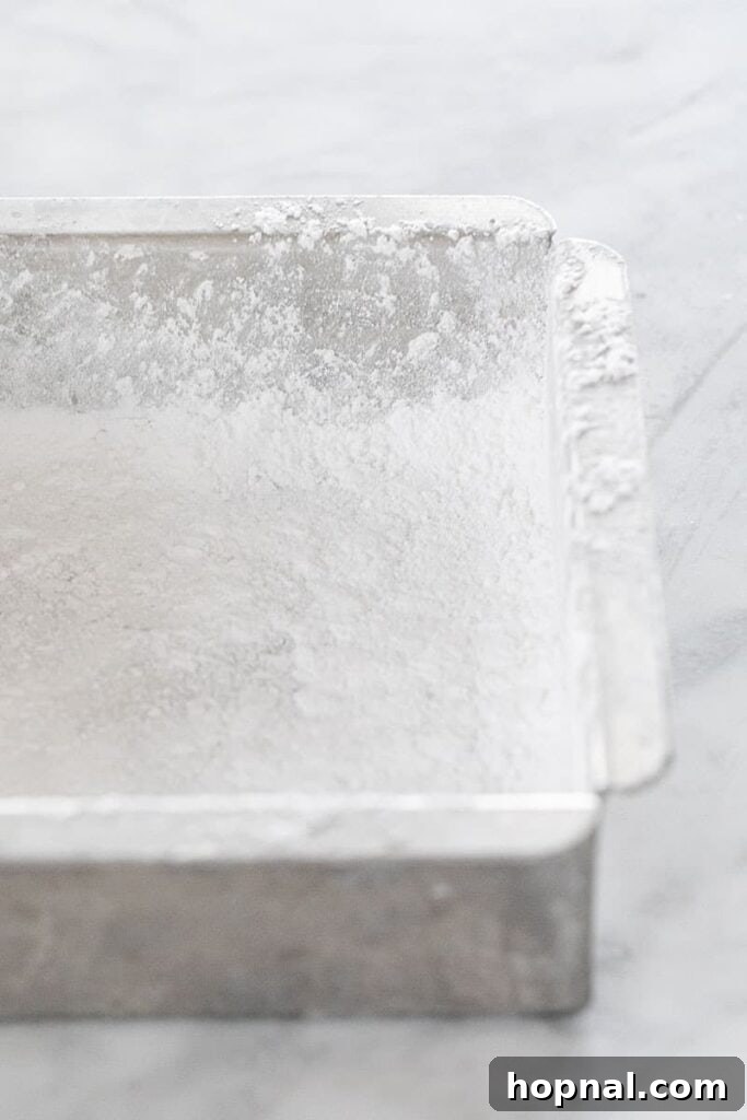 Püfür Püfür Ev Yapımı Marshmallow Sırları 4 A baking pan is meticulously prepared with a generous dusting of powdered sugar, creating a non-stick surface for the marshmallow mixture to prevent sticking.