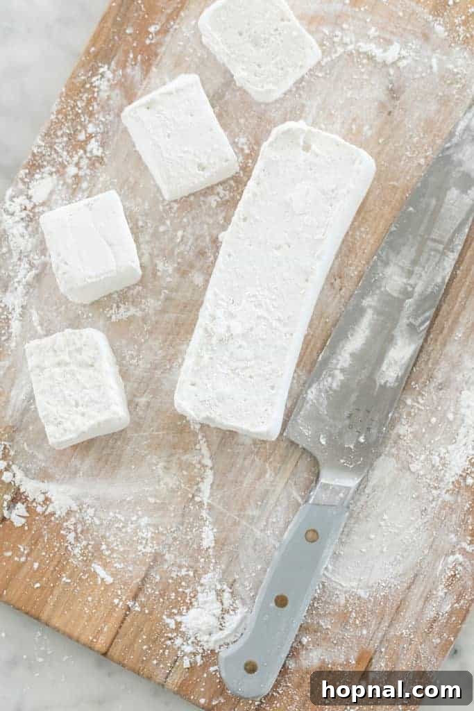 Püfür Püfür Ev Yapımı Marshmallow Sırları 9 A sheet of perfectly set, fluffy homemade marshmallows is carefully sliced into uniform squares on a cutting board using a sharp, dusted knife to prevent sticking.