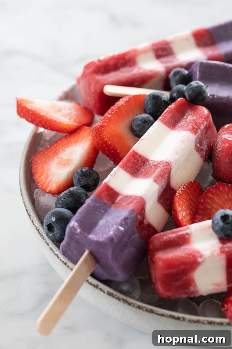 Striped red, white, and blue Bomb Pop popsicle with fresh strawberries and blueberries on a bowl of ice, perfect for a 4th of July celebration.