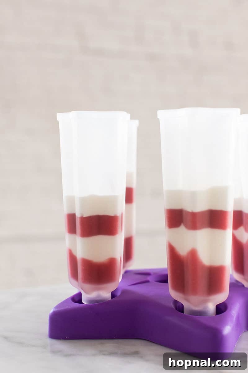 Popsicle molds filled with distinct red, white, and blue layers, showing the freezing process for a classic Bomb Pop design.