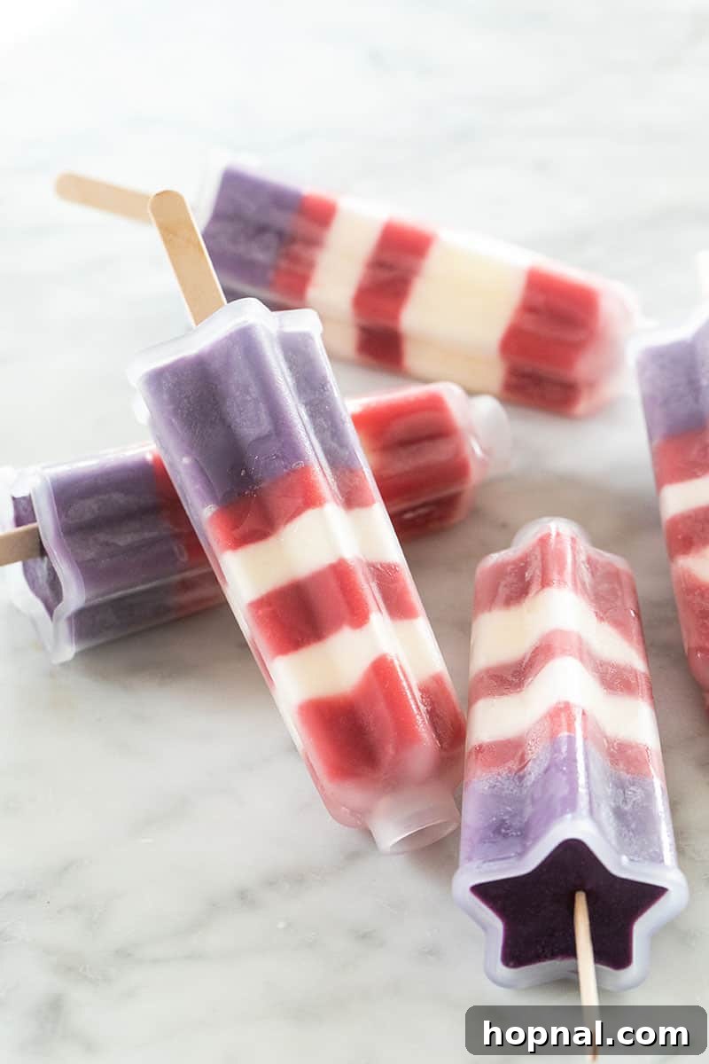 A hand gently arranging popsicle sticks into a mold filled with layers, demonstrating the assembly process for homemade Bomb Pops.