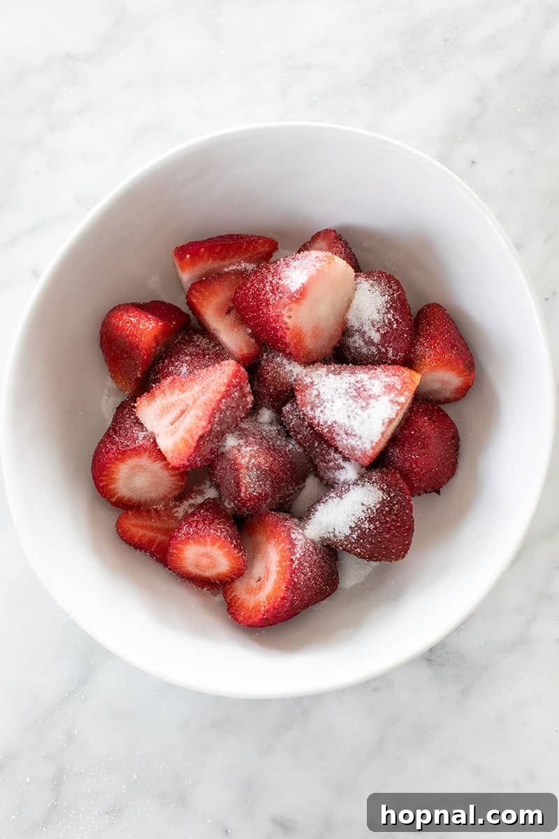 Fresh strawberries mixed with granulated sugar in a white bowl, preparing for the red layer of popsicles.