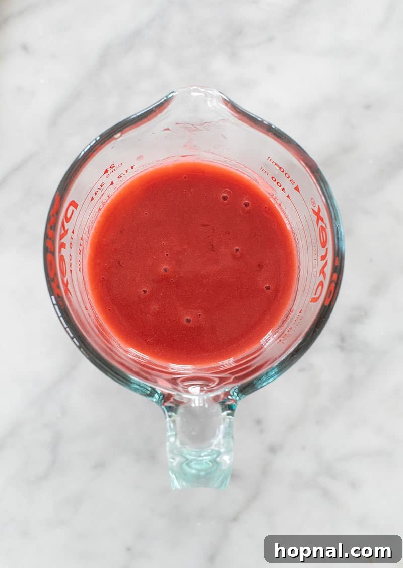 Close-up of the smooth, vibrant red strawberry popsicle mixture in a blender, ready for pouring.