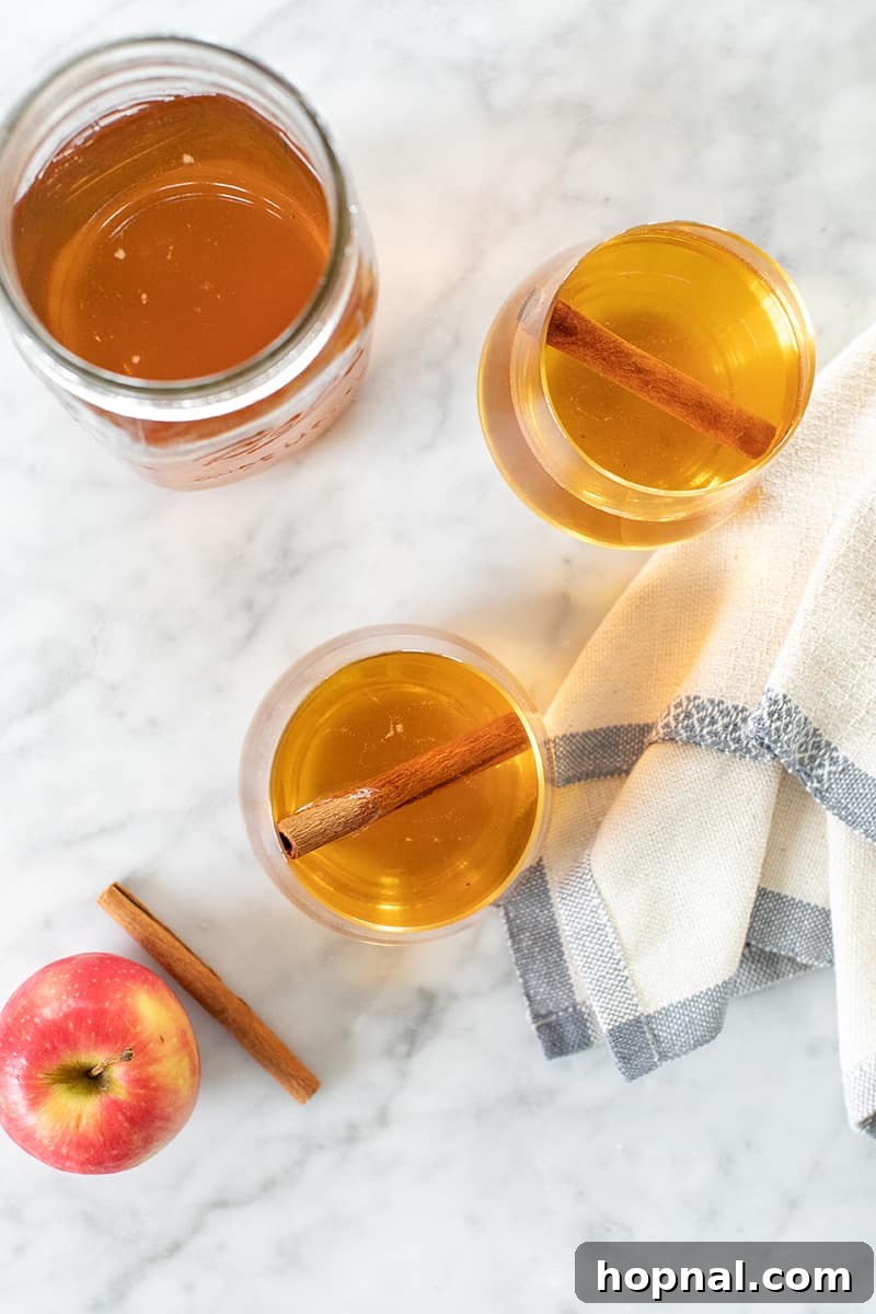 Two elegant cups of apple pie moonshine garnished with cinnamon sticks, alongside a sealed jar of moonshine.