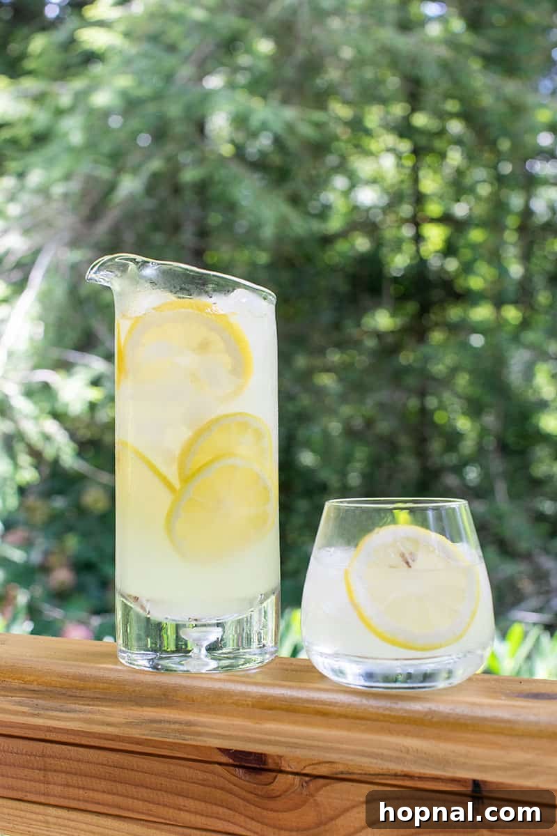 Zesty Homemade Lemonade Delight 4 A large glass pitcher filled with homemade lemonade, garnished with fresh lemon and lime slices, sitting on a table.