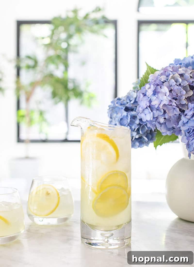 Zesty Homemade Lemonade Delight 5 Large pitcher of homemade lemonade garnished with lemon slices and mint, alongside glasses filled with ice and lemon.
