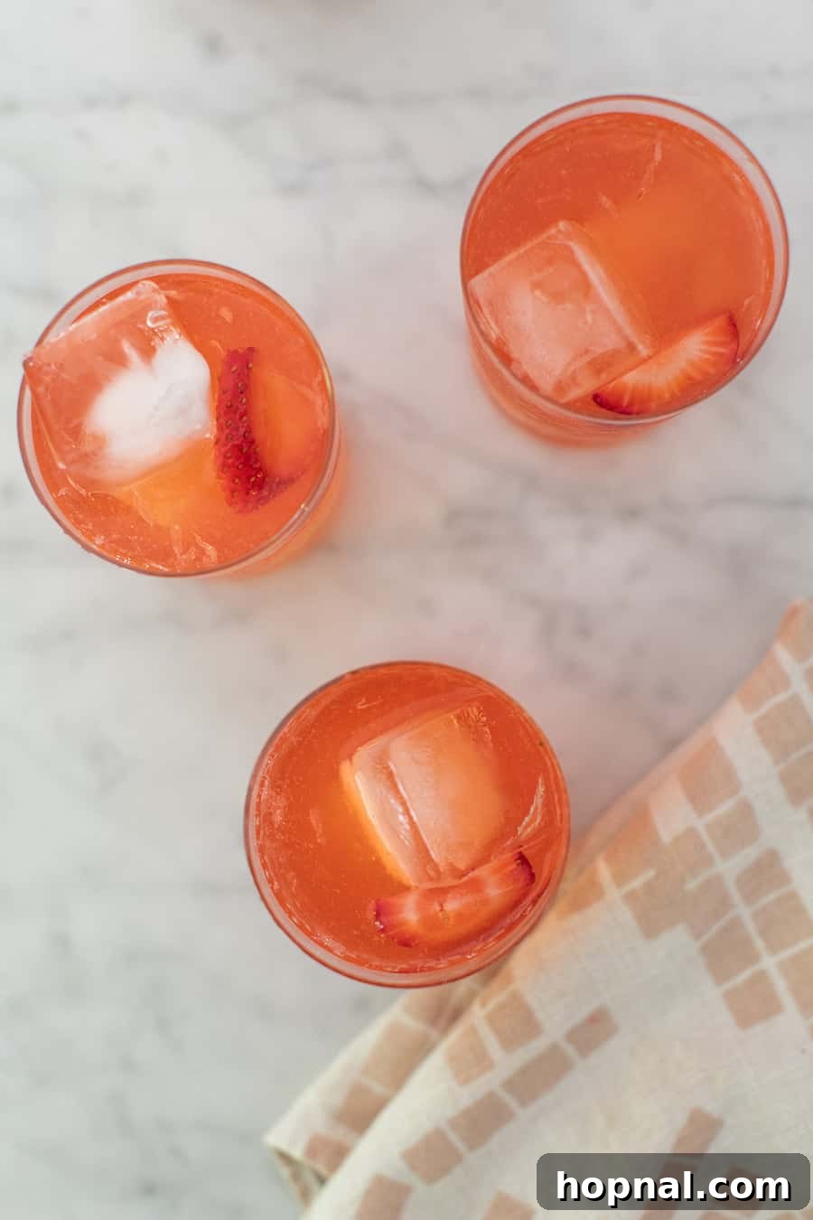 Multiple glasses of freshly made strawberry lemonade, garnished with fruit, on a table, ready for serving.