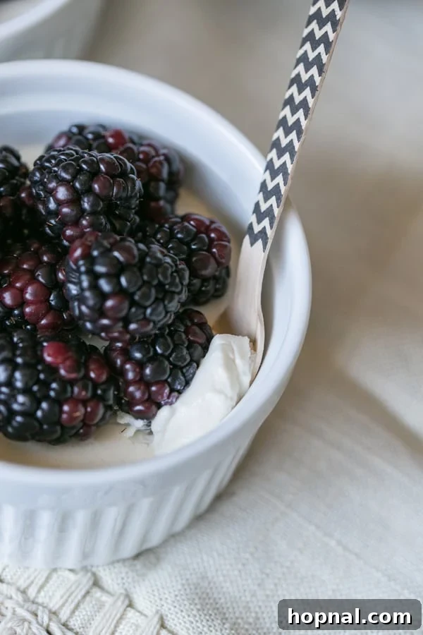 An overhead shot of a single serving of vanilla panna cotta in a white bowl, generously topped with fresh blackberries and mint leaves.