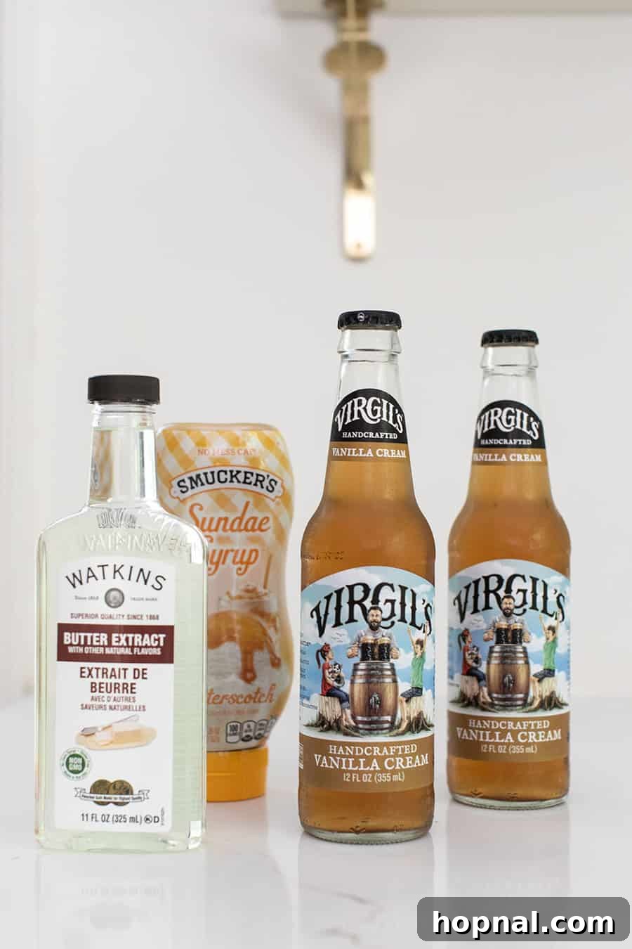 Ingredients for making homemade butterbeer: vanilla cream soda, butter extract, and butterscotch syrup displayed on a counter.
