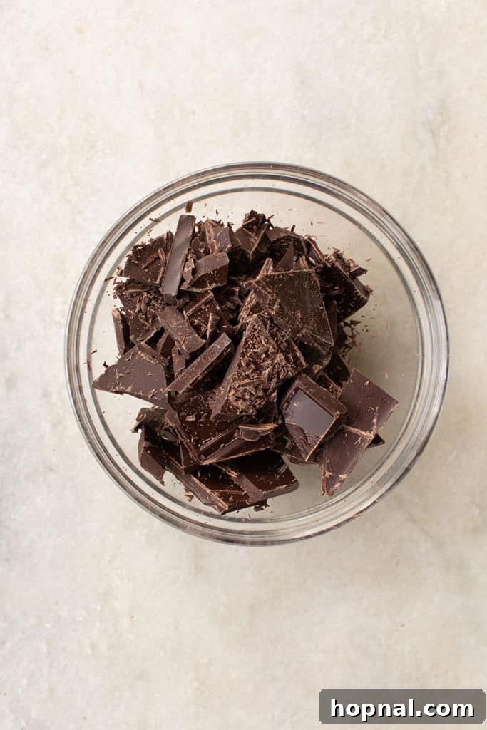 Finely chopped dark chocolate pieces ready to be added to the warm cream mixture, ensuring even melting.