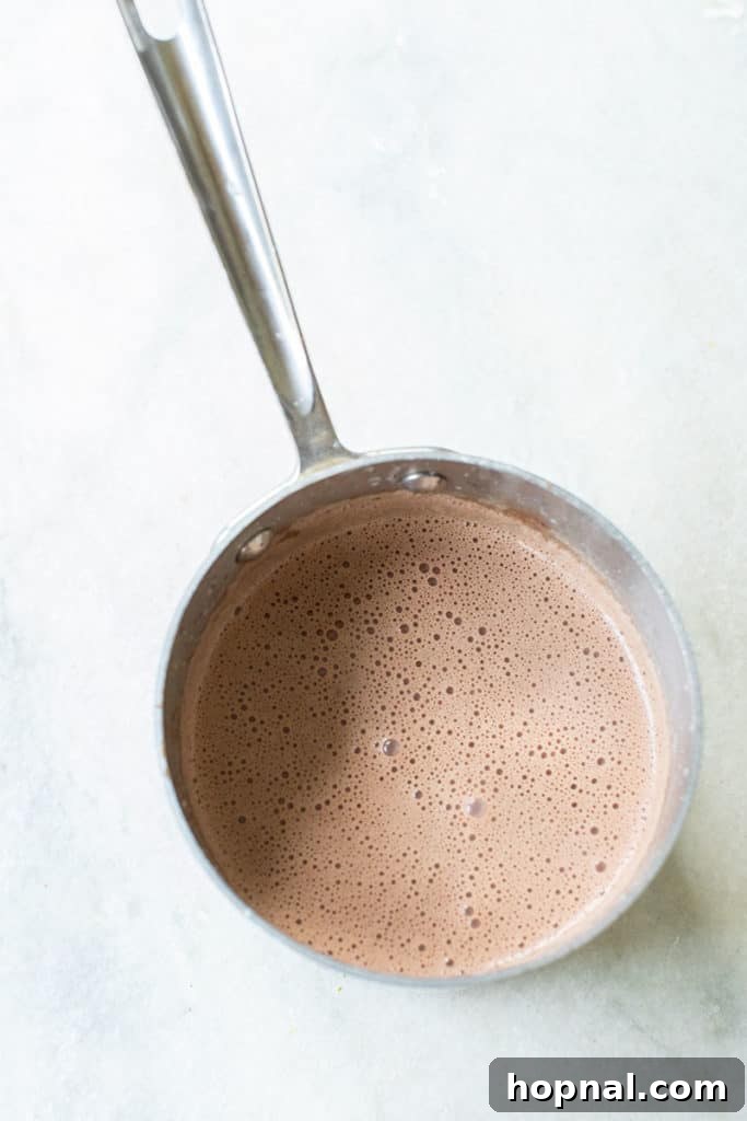 Dark chocolate melting smoothly into heavy cream in a saucepan over gentle heat, forming the rich base for the panna cotta.