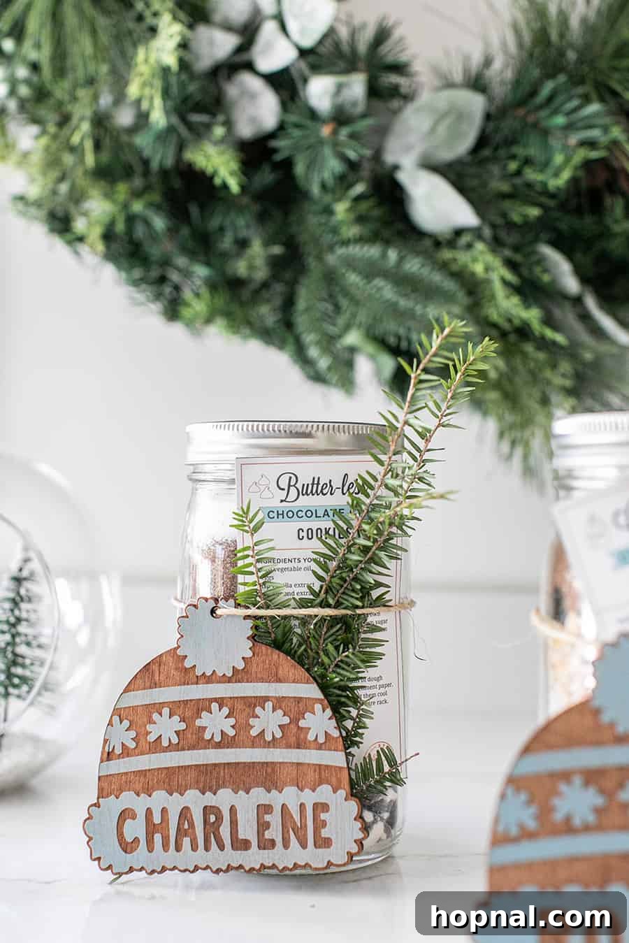 Beautifully crafted cookie mix in a jar, adorned with a personalized wooden Christmas tree ornament and twine, ready for holiday gifting.
