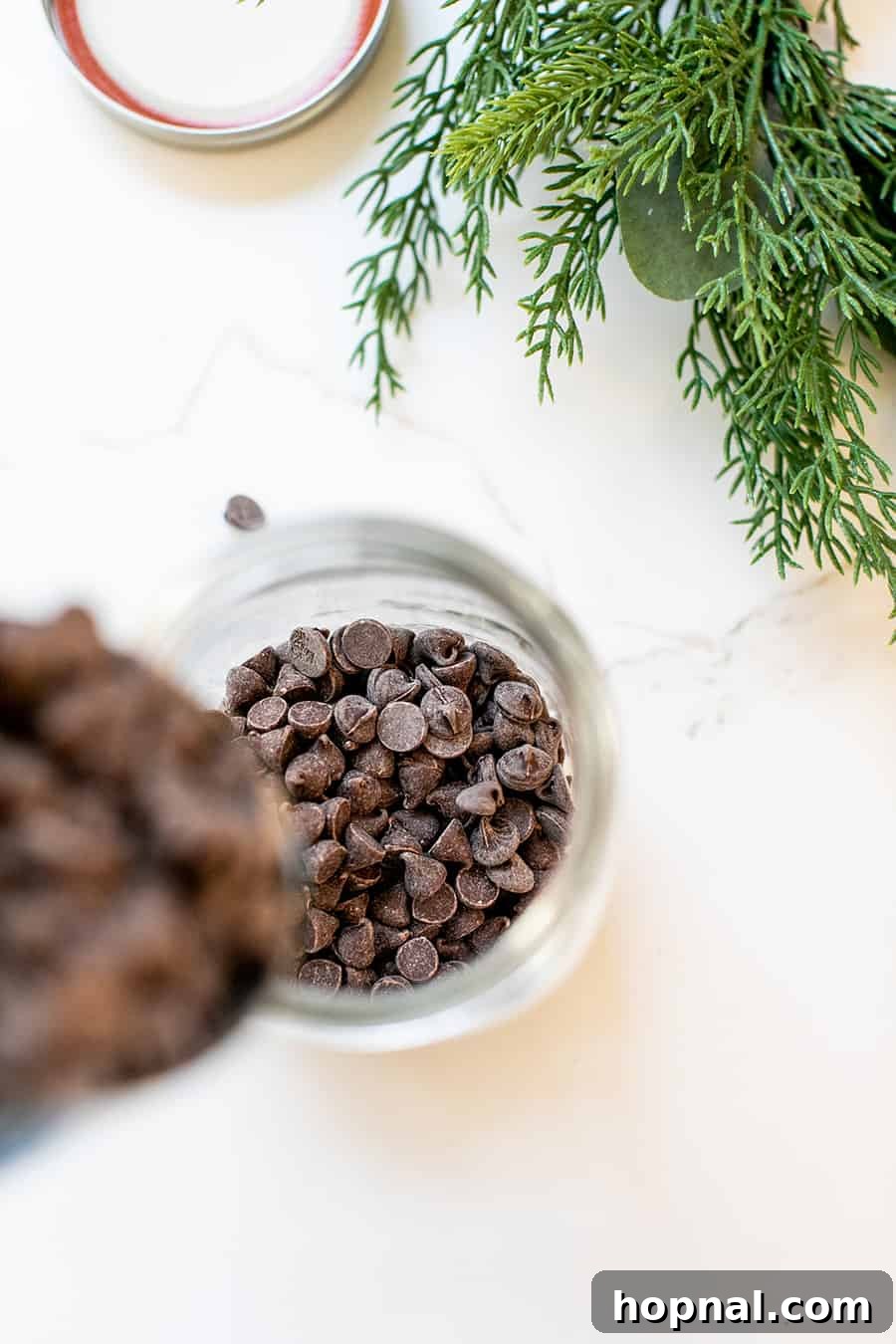 Delicious chocolate chips being poured into a wide-mouth glass jar, ready to be layered with other cookie mix ingredients.